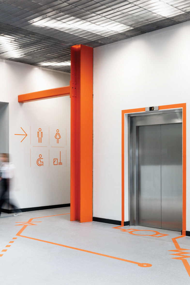 dnco_wayfinding - Publicidad Supra Hall con ascensor y acceso a los baños con decoración naranja